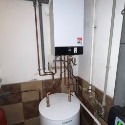 HYDROSTREFA ANDRZEJ SZCZĘSNY - Nowoczesny piec gazowy Viessmann z miedzianą instalacją, zamontowany w pomieszczeniu z częściowo wykończonymi ścianami i widocznym zasobnikiem wody.