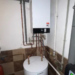Nowoczesny piec gazowy Viessmann z miedzianą instalacją, zamontowany w pomieszczeniu z częściowo wykończonymi ścianami i widocznym zasobnikiem wody.