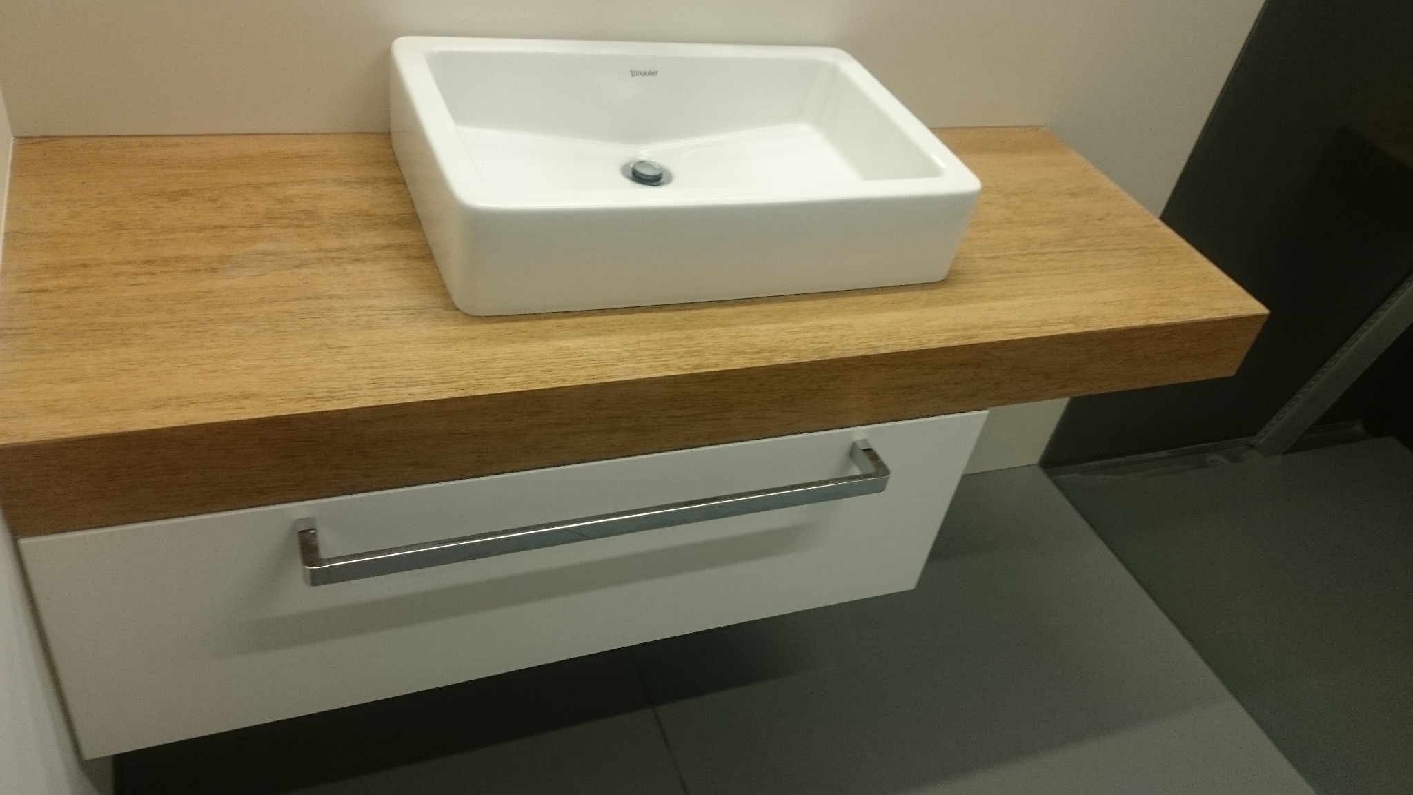 Nowoczesna umywalka nablatowa Duravit na drewnianym blacie z szufladą z chromowanym uchwytem, minimalistyczne wykończenie łazienki.