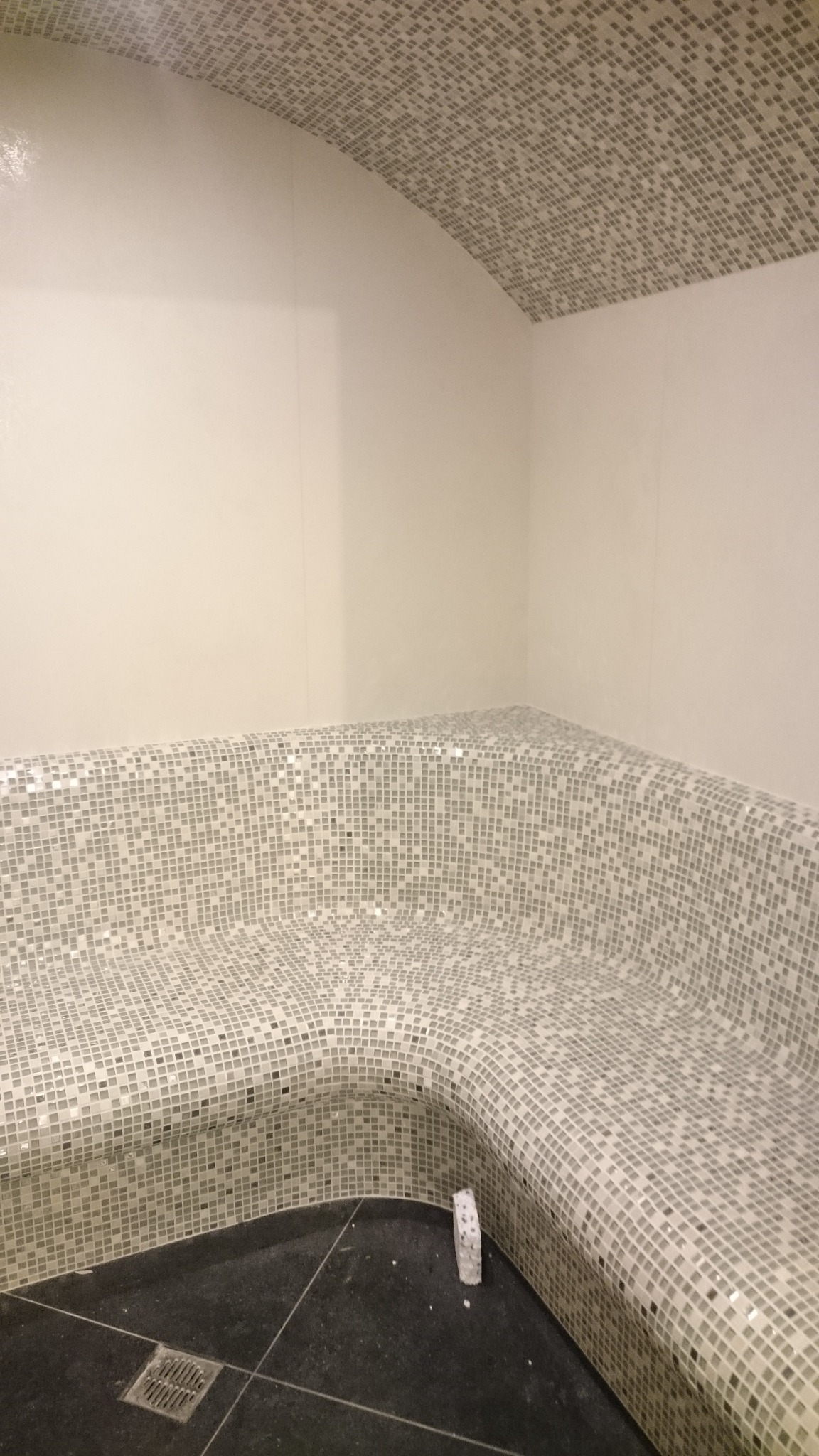 Wnętrze wykończonej łaźni parowej z mozaiką na suficie i siedzisku, czarna posadzka z kratką odpływową, widoczny fragment listwy przypodłogowej.