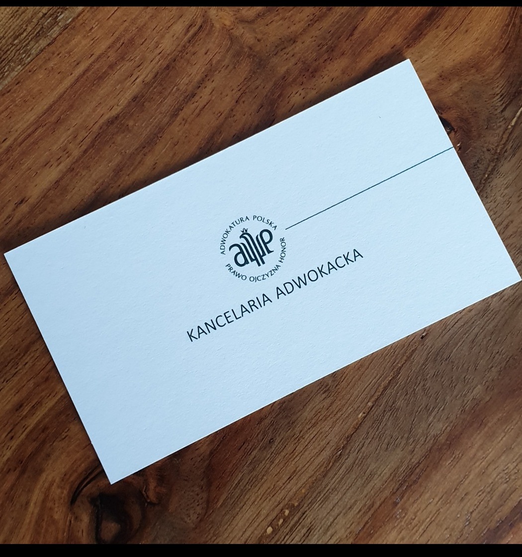 Wizytówka Kancelarii Adwokackiej z logo na drewnianym tle.