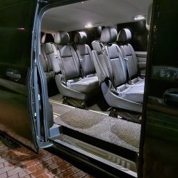 Konrad Bek TOURS STELABUS - Wnętrze przestronnego busa z czarnymi skórzanymi fotelami i otwartymi drzwiami, gotowego do komfortowego przewozu osób w Pogórze. Nocne oświetlenie.