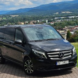 Konrad Bek TOURS STELABUS - Czarny van Mercedes-Benz z polską rejestracją na tle malowniczego krajobrazu górskiego i zabudowy miejskiej. Auto zaparkowane na brukowanej nawierzchni.