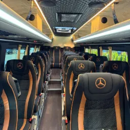 Luksusowe wnętrze busa Mercedes z czarno-pomarańczowymi fotelami z logo, oświetleniem LED i eleganckim wykończeniem sufitu. Komfort i prestiż w transporcie.