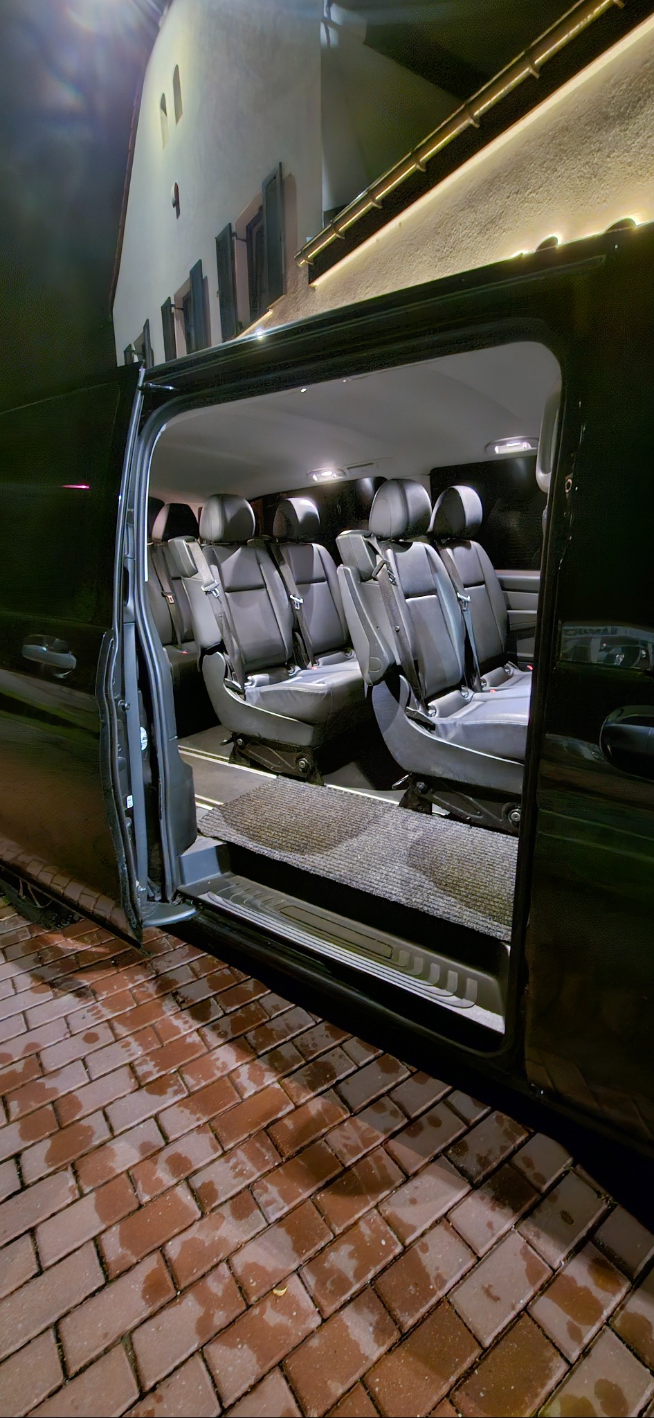 Wnętrze przestronnego busa z czarnymi skórzanymi fotelami i otwartymi drzwiami, gotowego do komfortowego przewozu osób w Pogórze. Nocne oświetlenie.