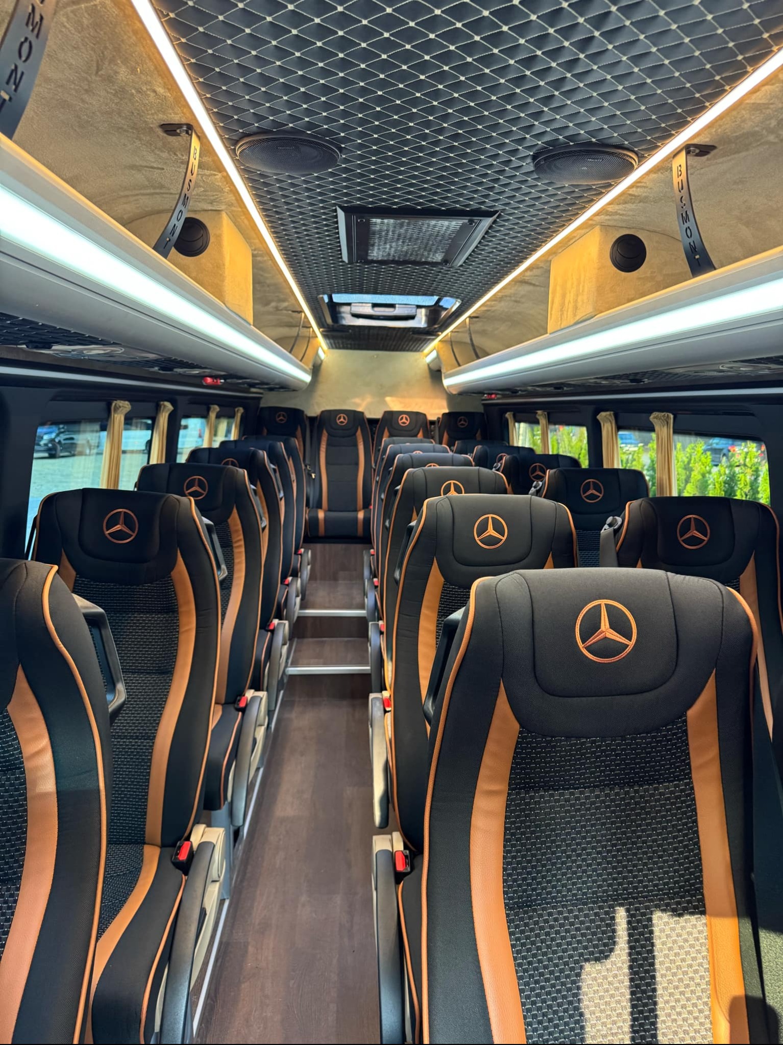 Luksusowe wnętrze busa Mercedes z czarno-pomarańczowymi fotelami z logo, oświetleniem LED i eleganckim wykończeniem sufitu. Komfort i prestiż w transporcie.