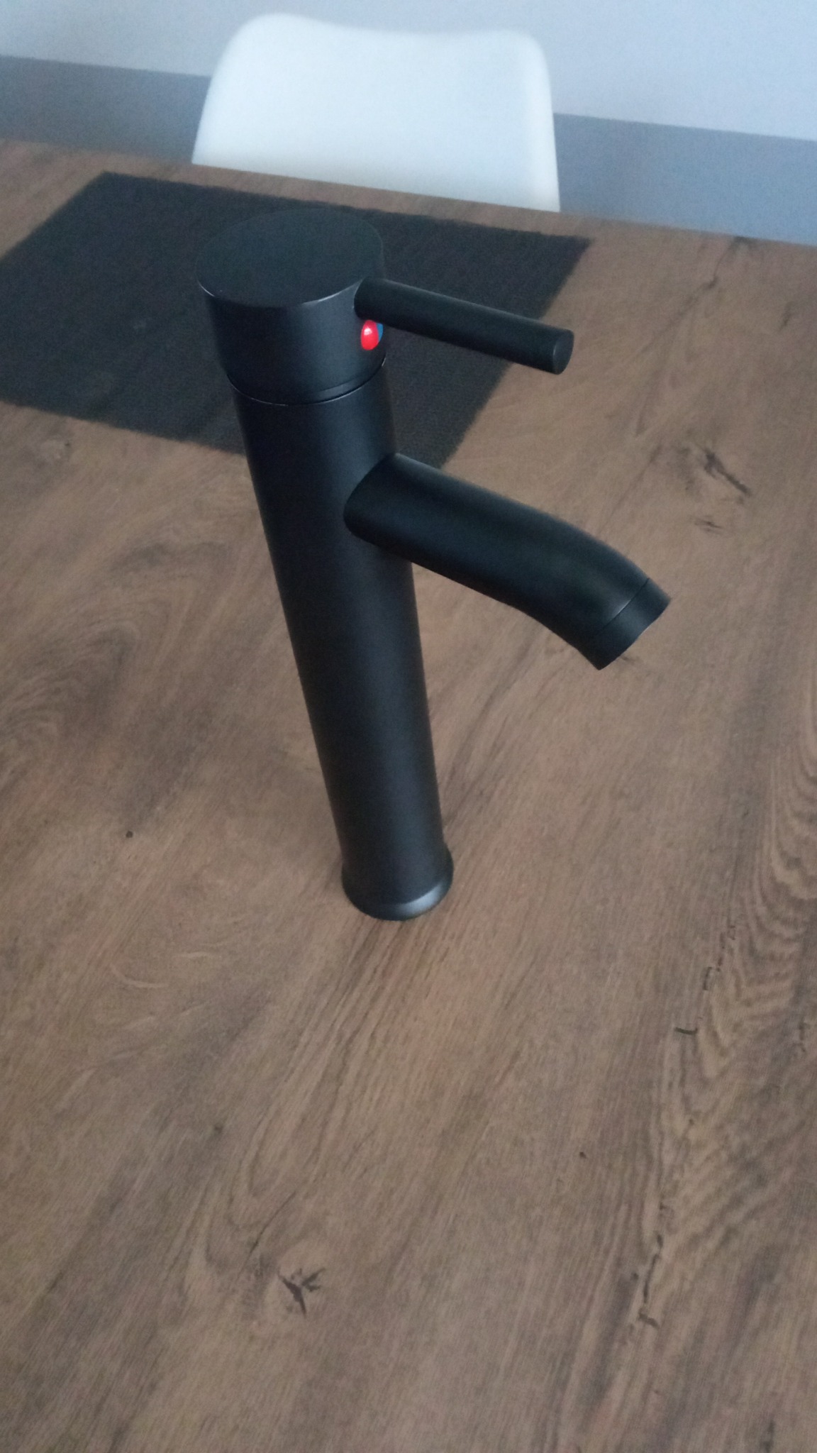 Wysoka, matowa, czarna bateria umywalkowa stojąca na drewnianym blacie. Widoczny czerwony i niebieski wskaźnik temperatury.