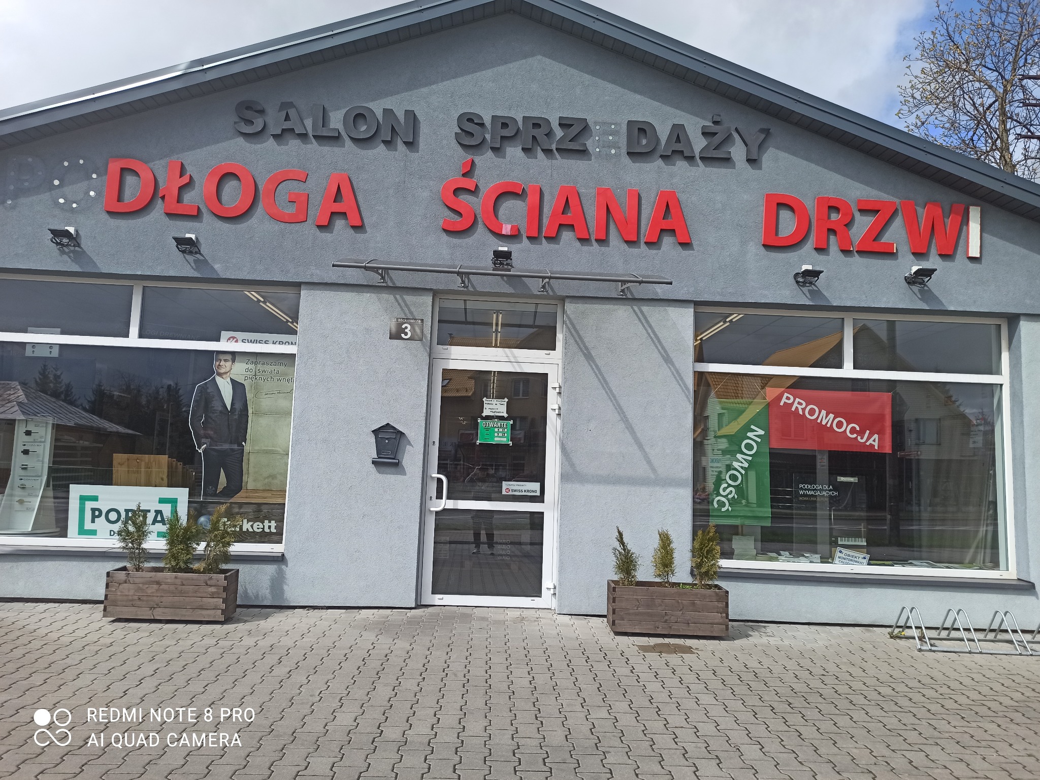 Fasada salonu sprzedaży drzwi 'Długa Ściana Drzwi' przy ulicy Mickiewicza 3 w Bielsku Podlaskim, z widocznymi ekspozycjami w oknach i informacją o promocji.