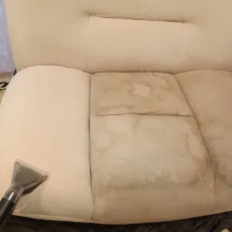 Fragment sofy z widoczną różnicą w czystości tapicerki po lewej stronie i zabrudzeniami po prawej, czyszczona ssawką odkurzacza piorącego.