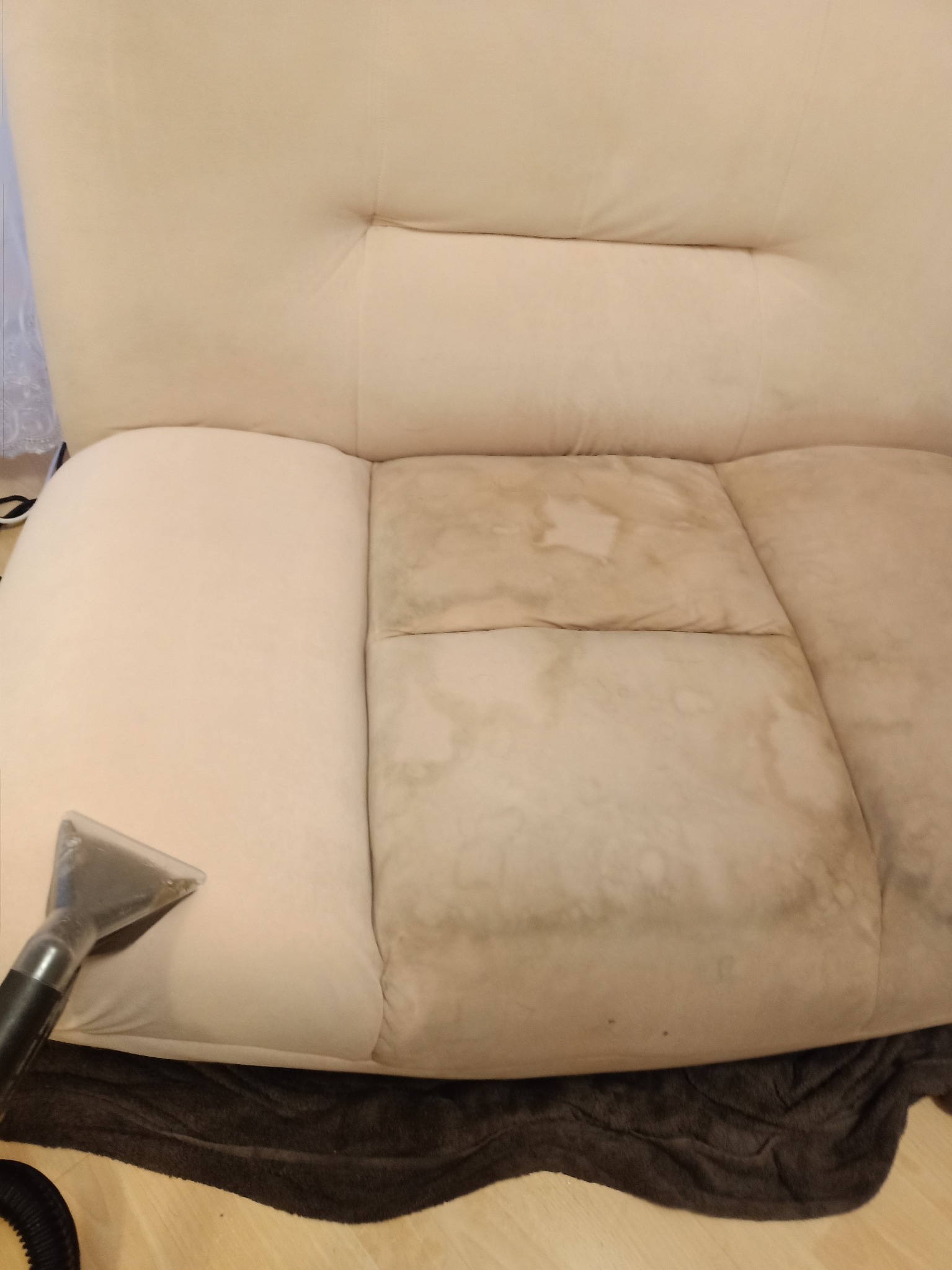 Fragment sofy z widoczną różnicą w czystości tapicerki po lewej stronie i zabrudzeniami po prawej, czyszczona ssawką odkurzacza piorącego.