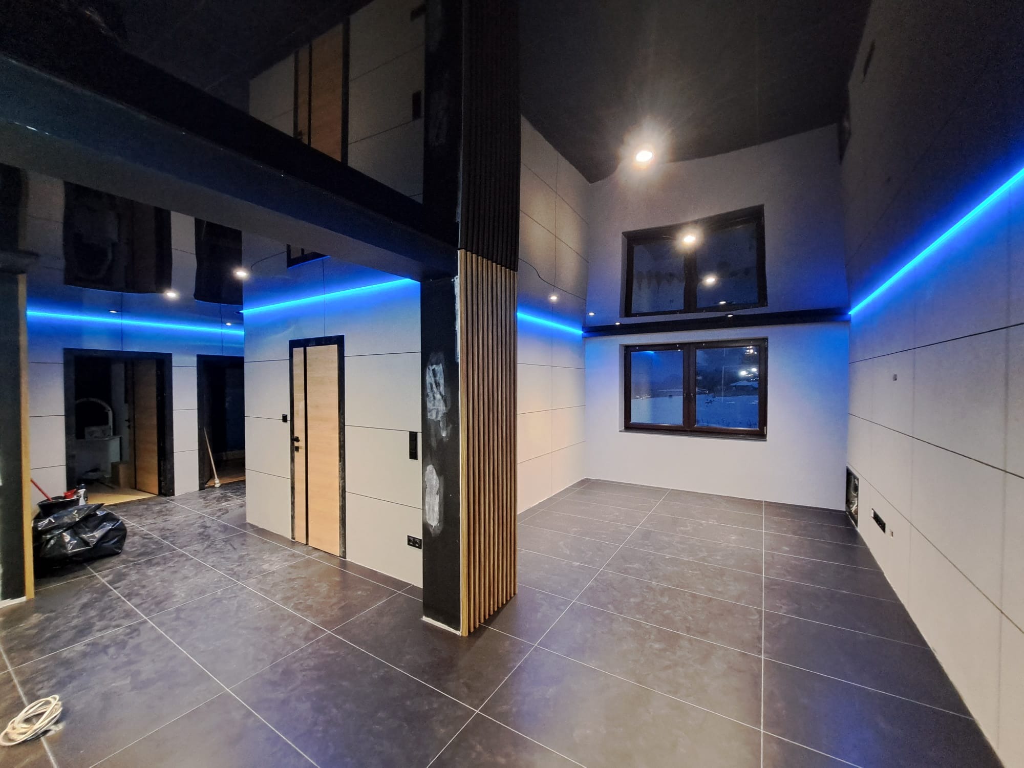 Wnętrze po remoncie z ciemną podłogą, białymi płytkami ściennymi, czarnym sufitem i niebieskim oświetleniem LED. Widoczny element dekoracyjny z drewnianych listew na filarze.