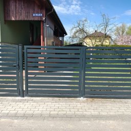 WILK - KOP ROBOTY ZIEMNE USŁUGI MINIKOPARKĄ PAWEŁ WILK - Nowoczesne, poziome ogrodzenie panelowe w kolorze grafitowym z furtką i bramą wjazdową na posesji z kostką brukową, widok z zewnątrz.