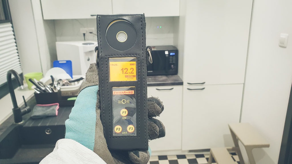 Pomiar poziomu ozonu w pomieszczeniu za pomocą urządzenia EWIWAR+WB, widoczny zlew z naczyniami w tle.