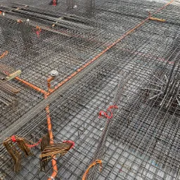 Siatka zbrojeniowa z pomarańczowymi rurami instalacyjnymi ułożona na przygotowanym podłożu, widoczne elementy mocujące i wystające pręty.