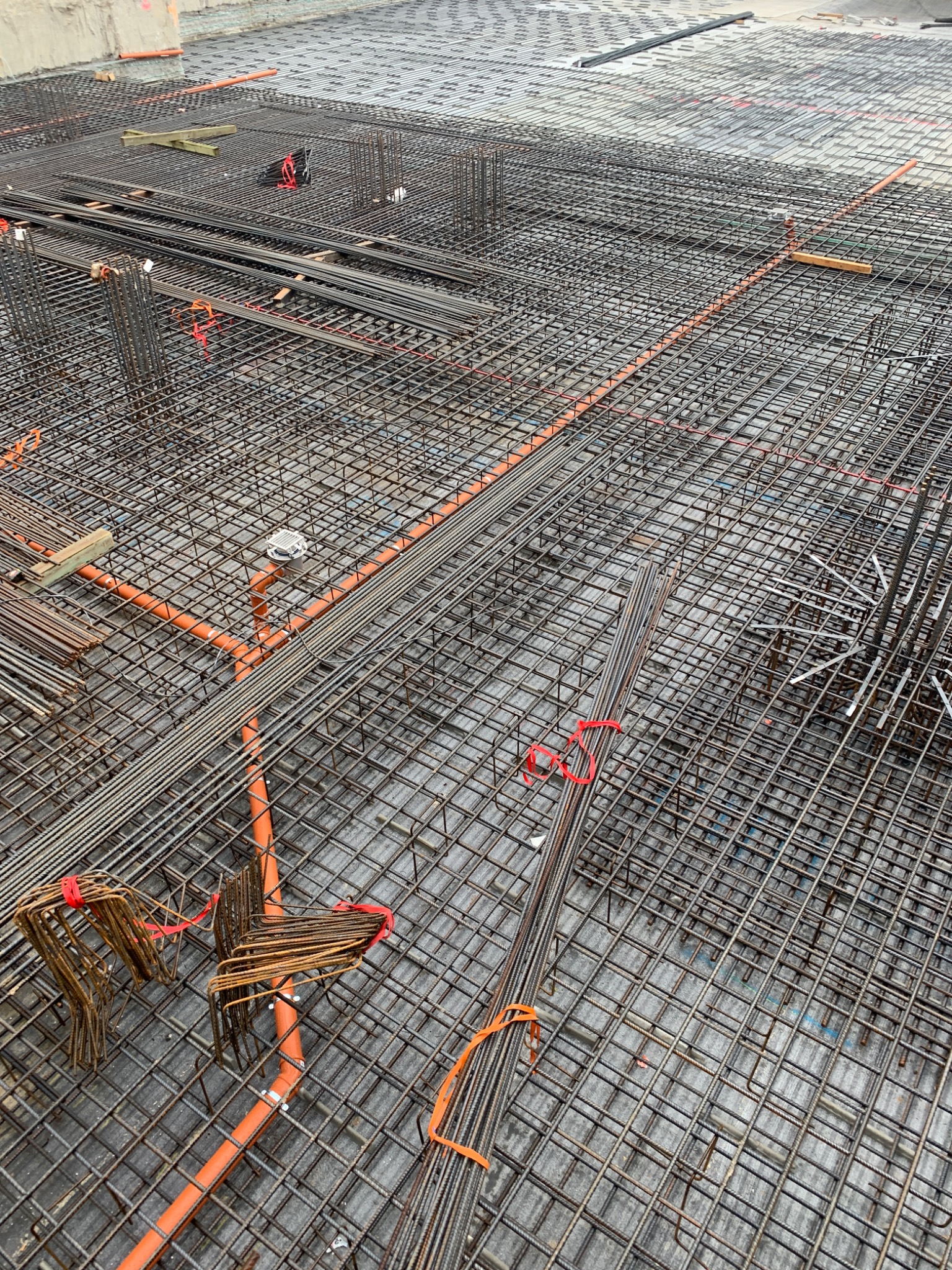 Siatka zbrojeniowa z pomarańczowymi rurami instalacyjnymi ułożona na przygotowanym podłożu, widoczne elementy mocujące i wystające pręty.