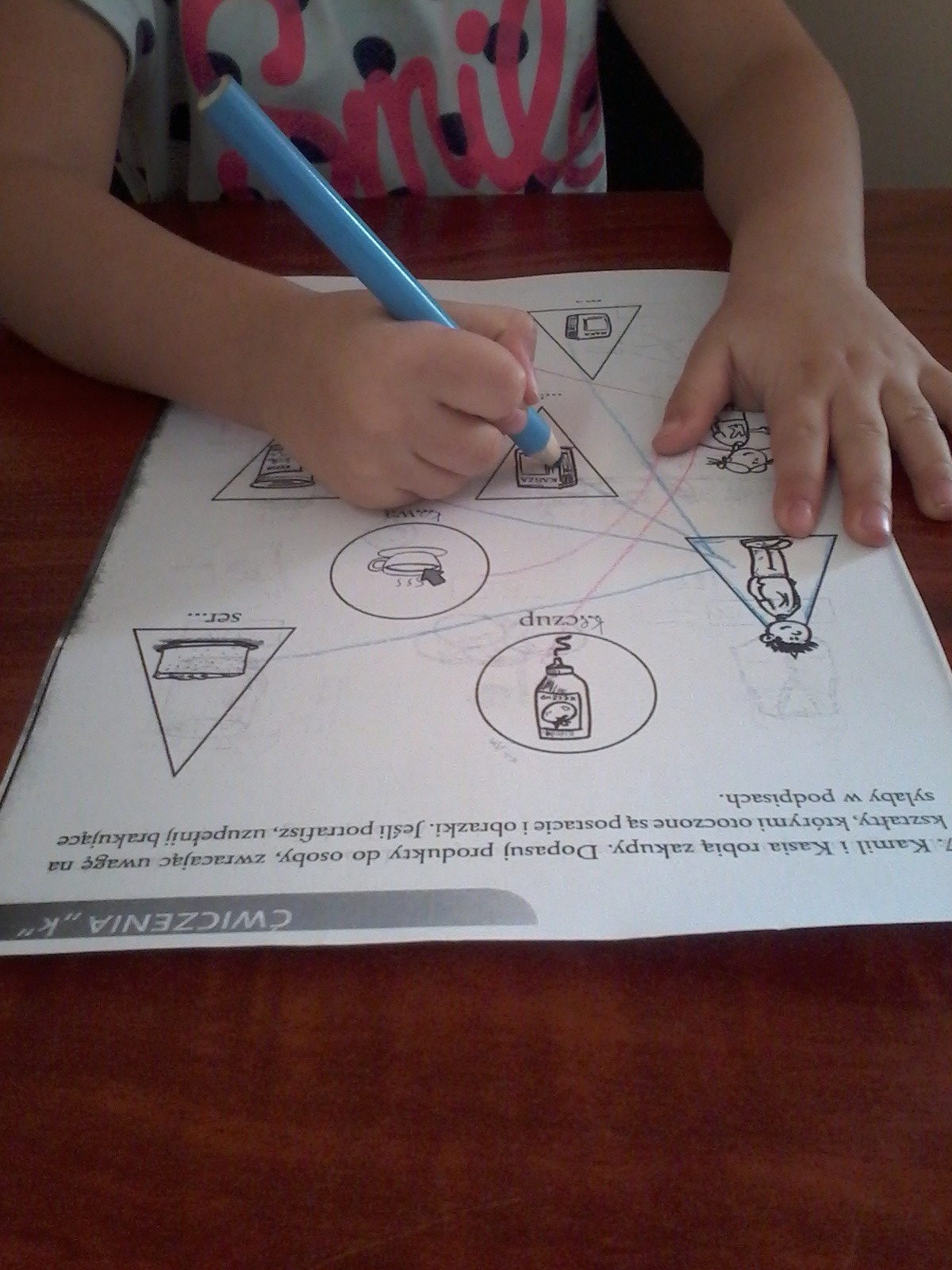 Dziecko wykonuje ćwiczenia logopedyczne w zeszycie, łącząc obrazki z odpowiednimi słowami za pomocą niebieskiego pisaka.