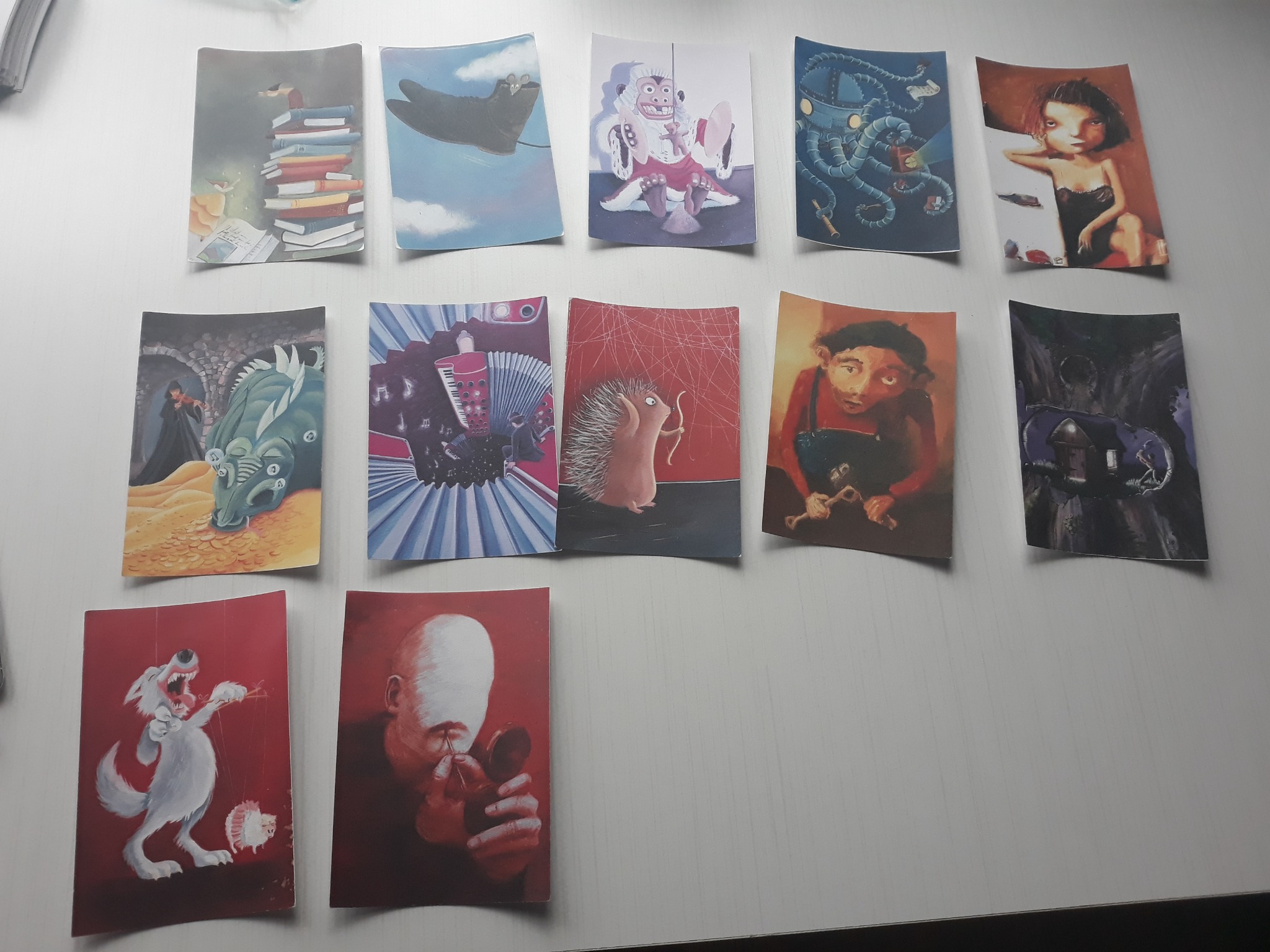 Kolekcja ilustracji na papierze, prezentujących różnorodne sceny i postacie, w tym stos książek, fantastyczne stworzenia, postacie z instrumentami i portrety, ułożonych na białym tle.