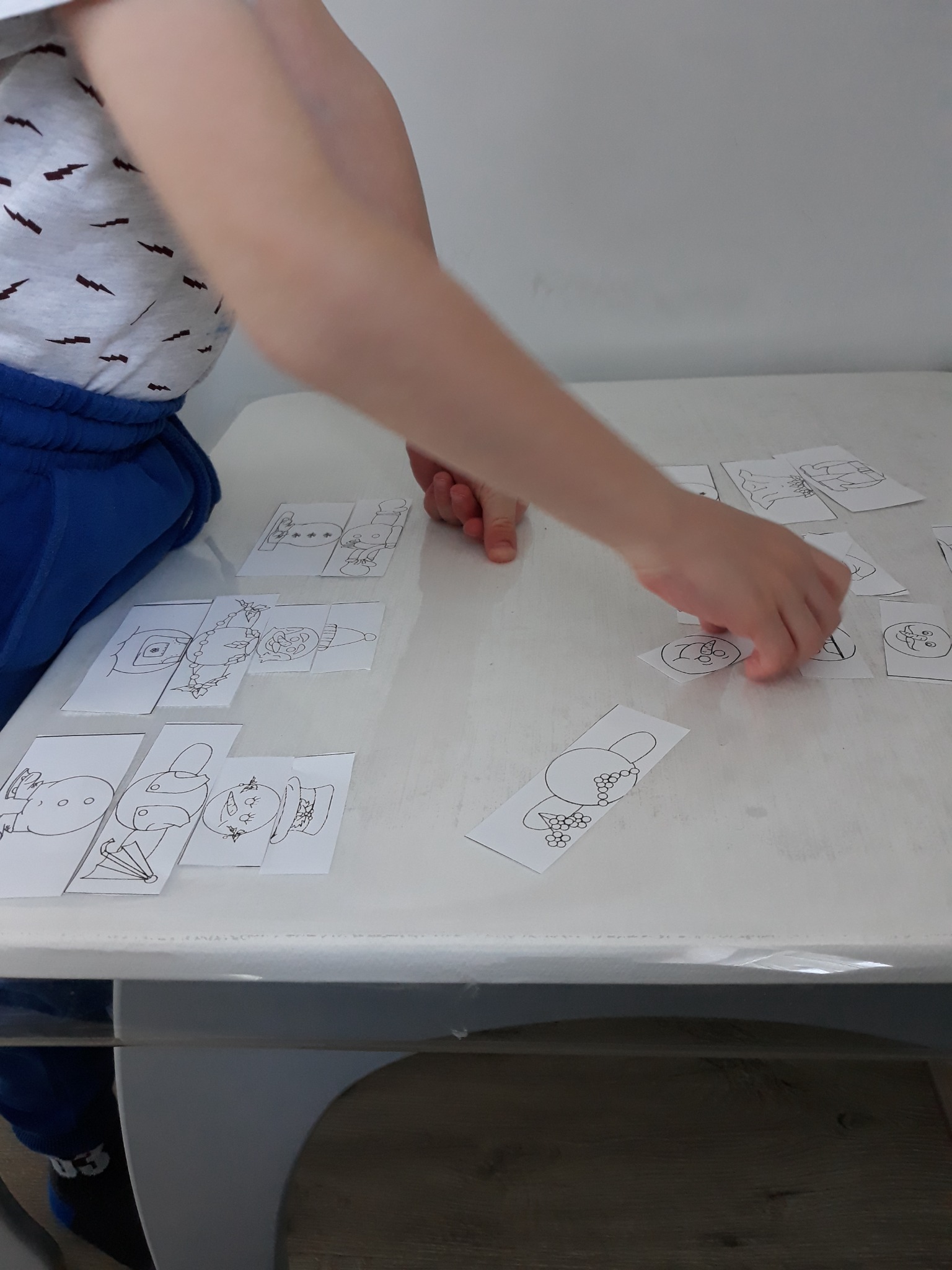 Dziecko układa puzzle obrazkowe z narysowanymi postaciami na białym stole.