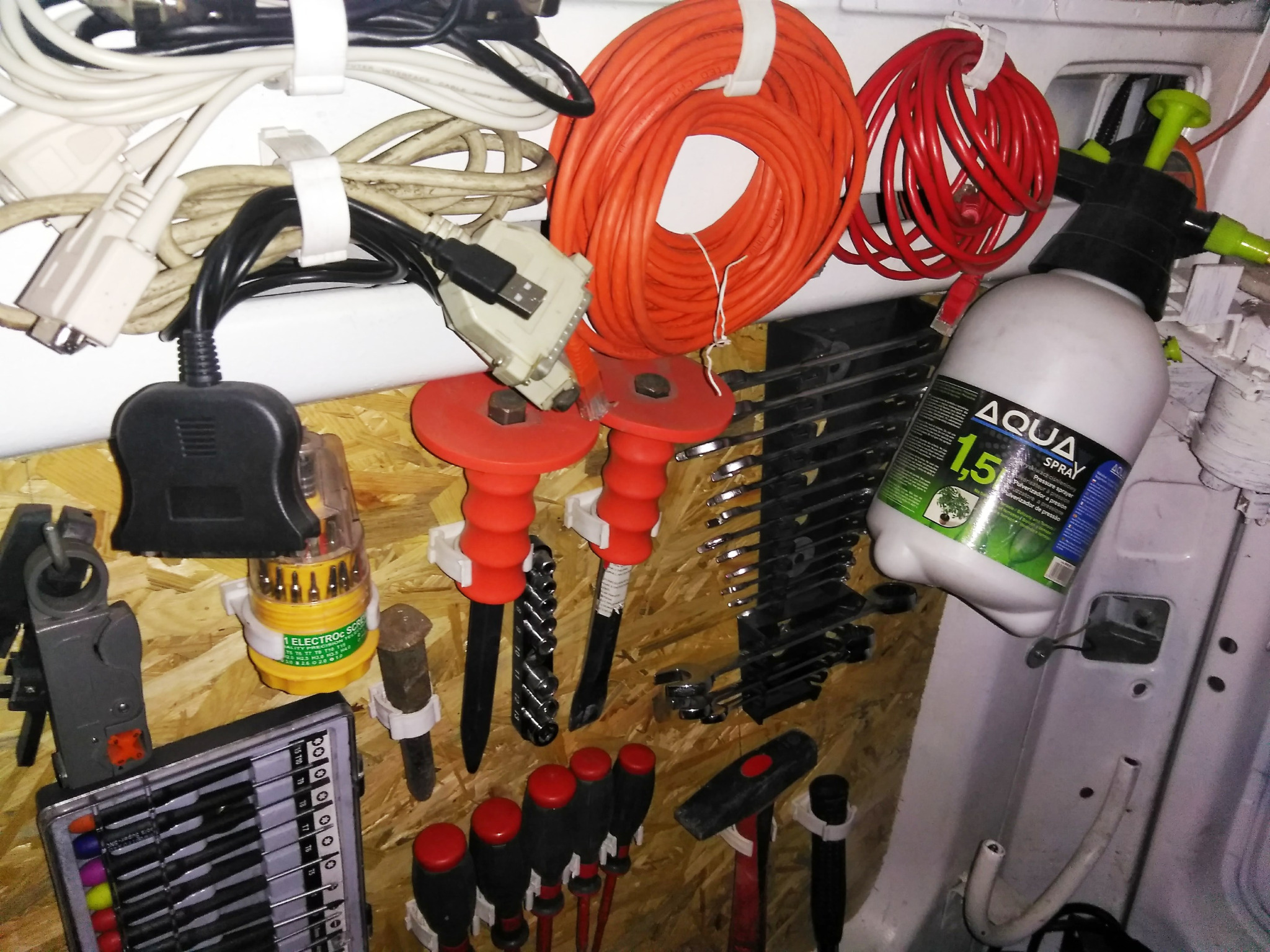 Wnętrze furgonetki zorganizowane jako warsztat mobilny; widoczne zwinięte kable elektryczne pomarańczowe i czerwone, narzędzia, wkrętaki, zestaw kluczy, spryskiwacz ciśnieniowy Aqua 1.5l, wszystko...