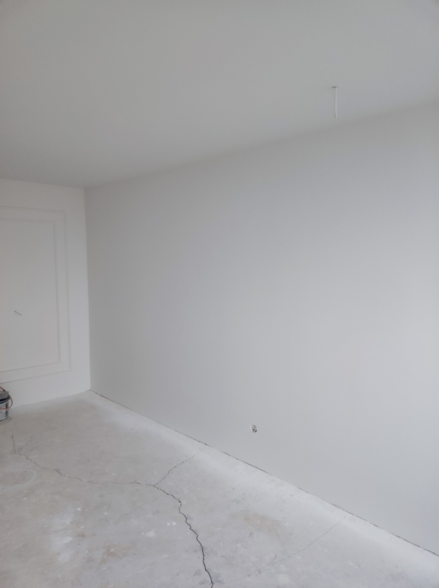 Białe, świeżo wykończone wnętrze pokoju z widocznymi pęknięciami na podłodze i delikatną sztukaterią przy ścianie, przygotowane do dalszych prac wykończeniowych.