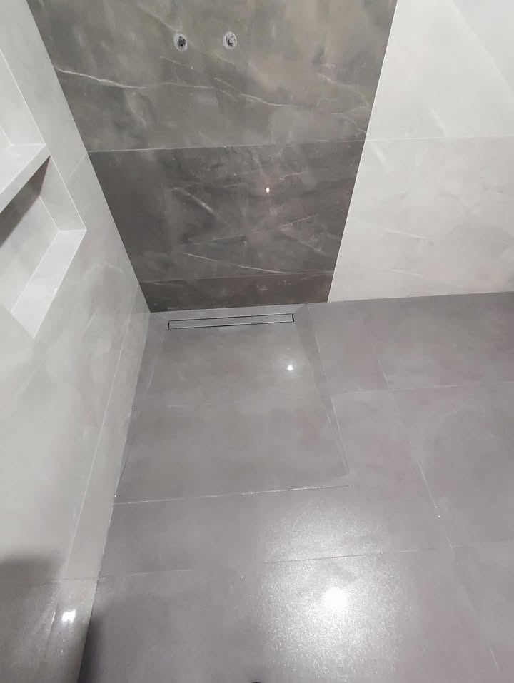 Nowoczesna łazienka z szarymi płytkami imitującymi marmur na ścianach i podłodze. Widoczny odpływ liniowy i wnęka w ścianie.