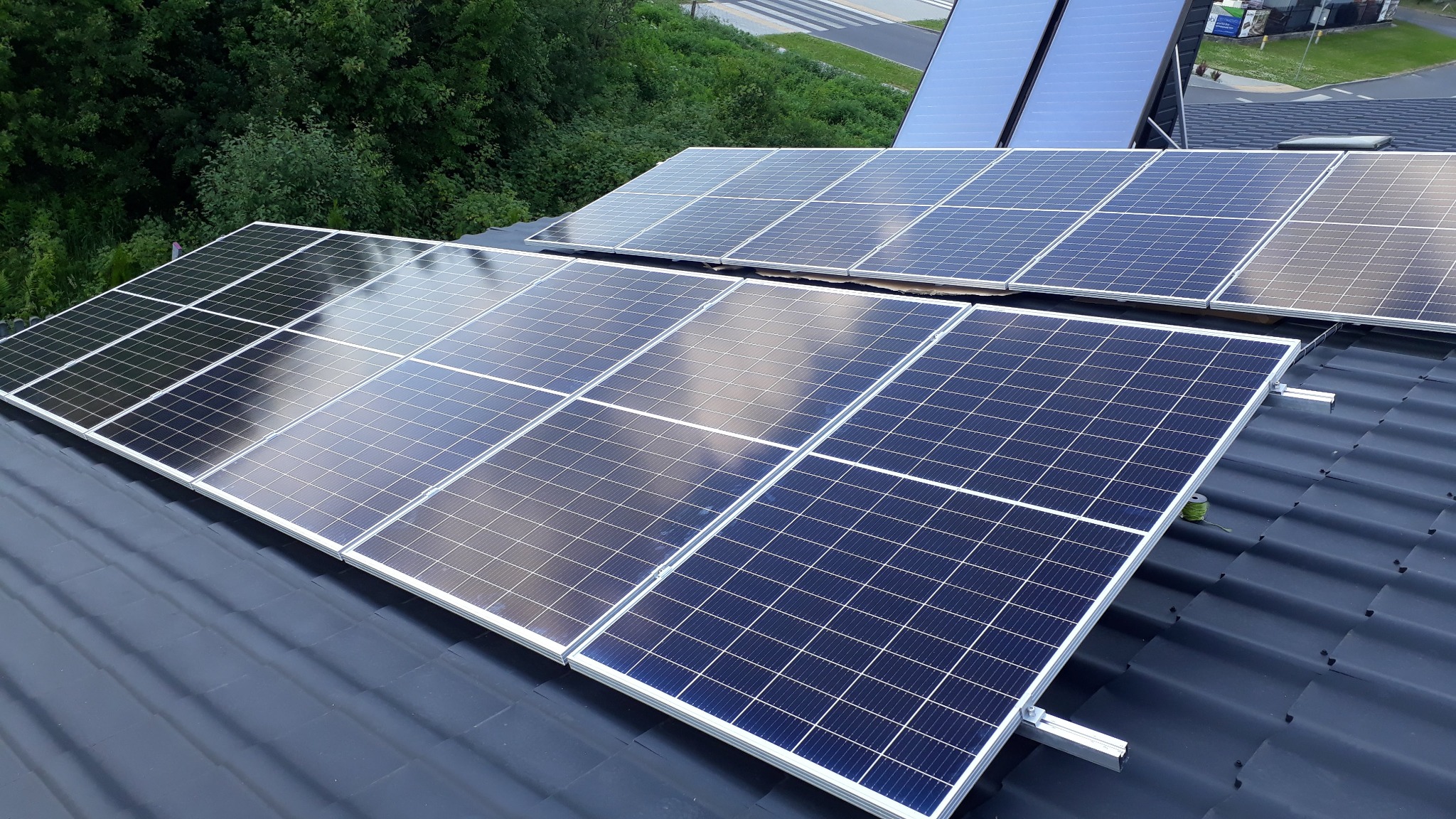 Panele słoneczne na grafitowym dachu z blachy, widoczne aluminiowe mocowania i zwój zielonego drutu.