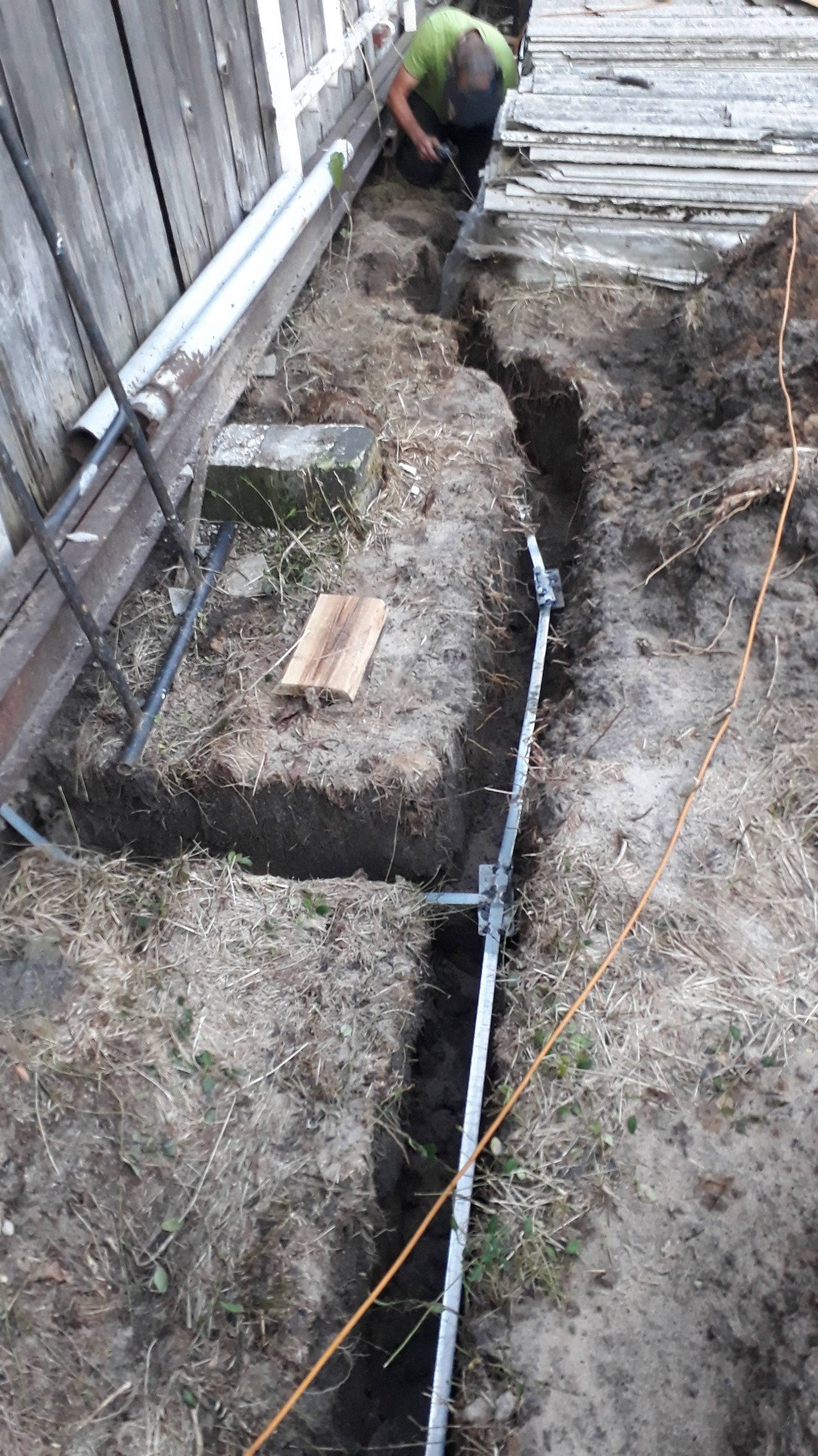 Wykop pod fundament z widoczną metalową konstrukcją wzmacniającą i pracownikiem wyrównującym dno, z widoczną deską i sznurkiem wyznaczającym linię.