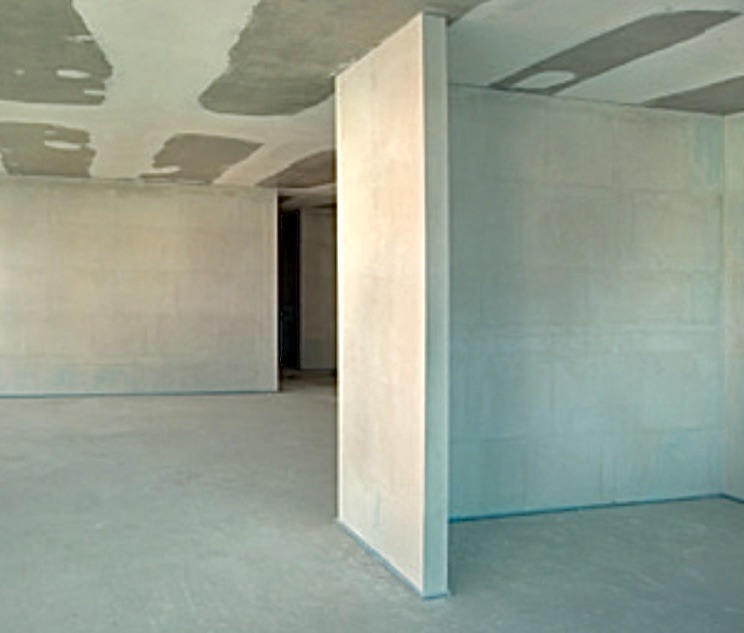 Surowe wnętrze z nowo wymurowanymi ścianami działowymi, widoczne ślady zaprawy na suficie, przygotowane do dalszych prac wykończeniowych.