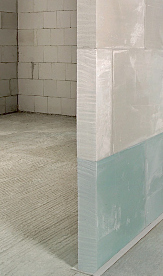 Fragment murowanej ściany z betonu komórkowego z widoczną izolacją przeciwwilgociową w kolorze zielonym, w surowym stanie wykończenia.