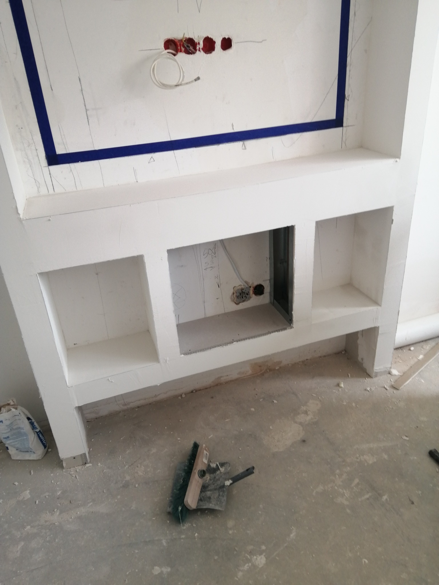 Wnęka ścienna z płyt karton gips i gładzią szpachlową, przygotowana do malowania, z widocznymi kablami elektrycznymi i narzędziami na podłodze.