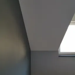 Poddasze po malowaniu: szara ściana, biały sufit skośny i okno wnękowe z widocznym parapetem.