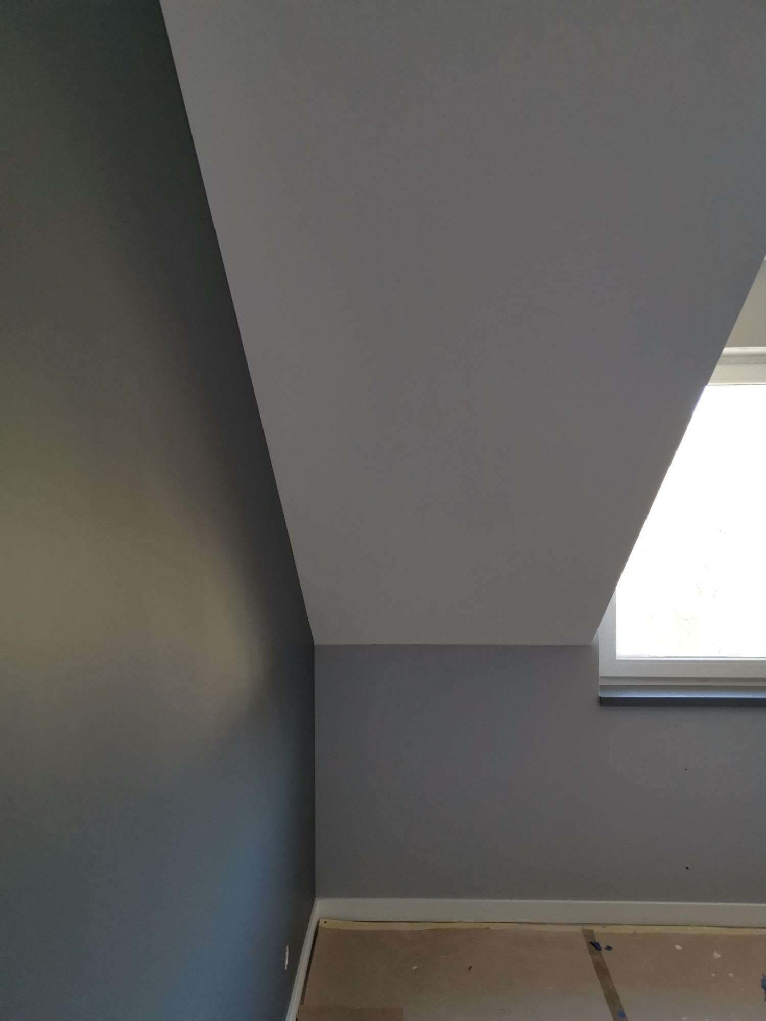 Poddasze po malowaniu: szara ściana, biały sufit skośny i okno wnękowe z widocznym parapetem.