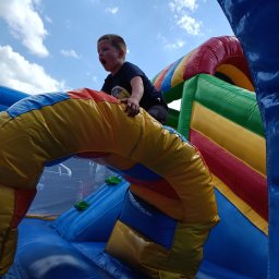 Bajlandia - Chłopiec z otwartymi ustami wspina się na kolorowy dmuchany zamek na tle nieba z chmurami. Widok z dołu, intensywne barwy.