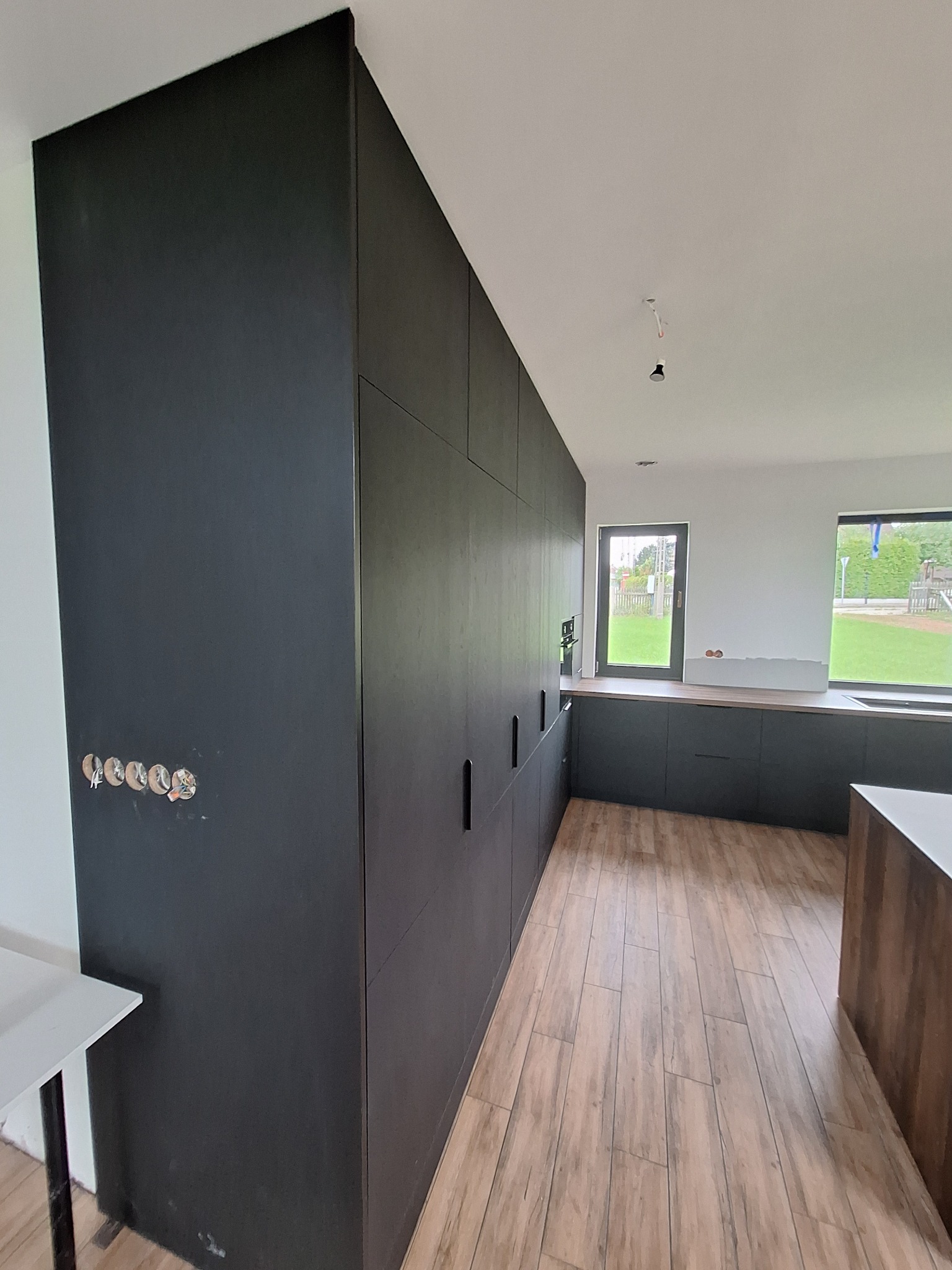 Ciemna zabudowa kuchenna w Rybniku, widoczne niedokończone wykończenia elektryczne na ścianie, podłoga imitująca drewno, okna z widokiem na ogród.