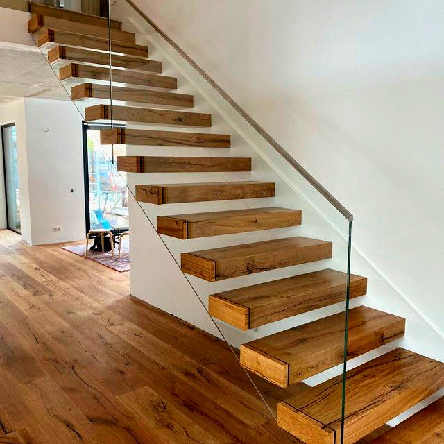 Nowoczesne, drewniane schody samonośne z przeszkloną balustradą, widok z dołu, ukazujący strukturę drewna i minimalistyczny design.