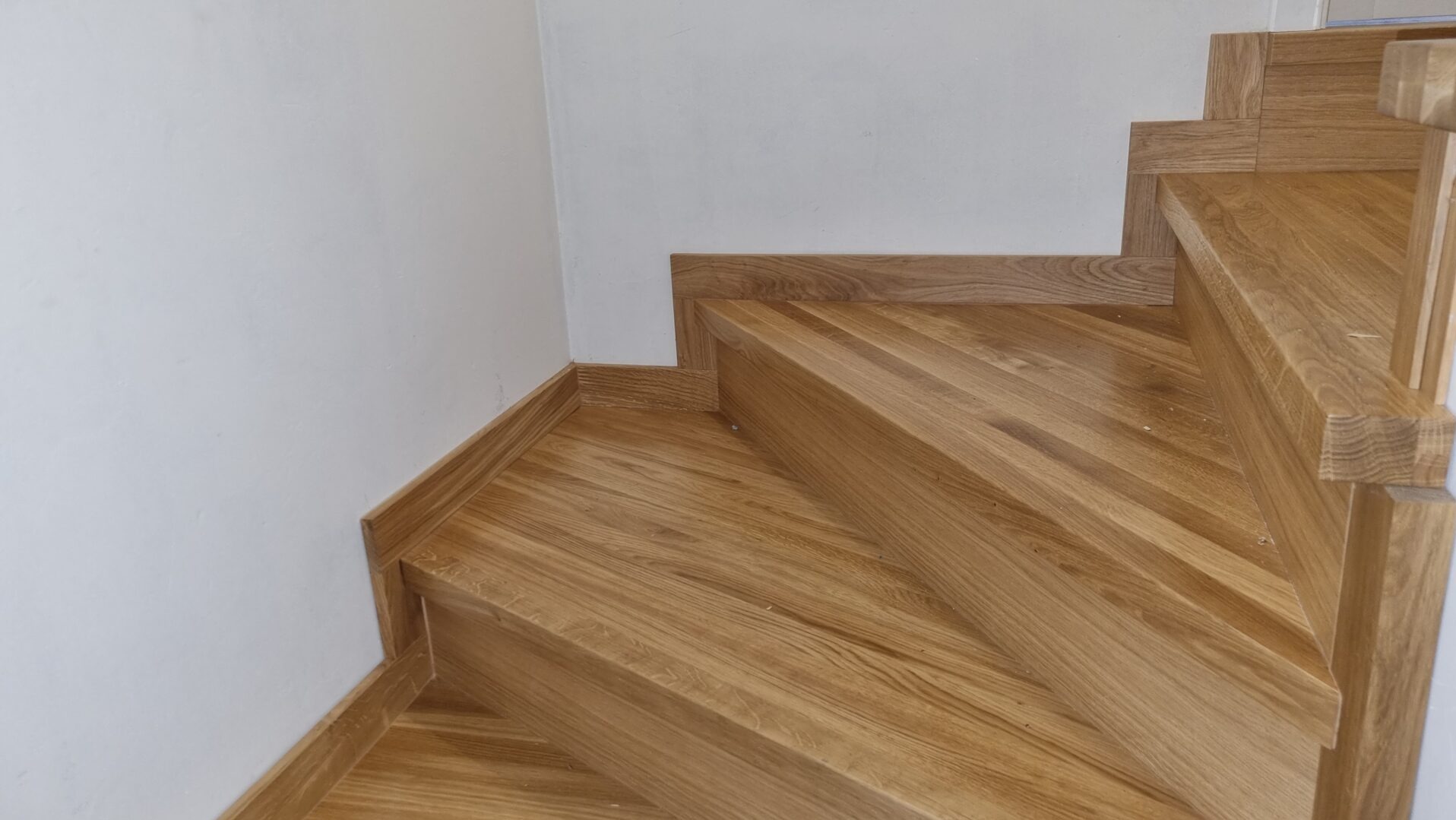 Drewniane schody z dębowymi stopniami i listwami przypodłogowymi, widok z dołu, jasne drewno z wyraźnym usłojeniem.