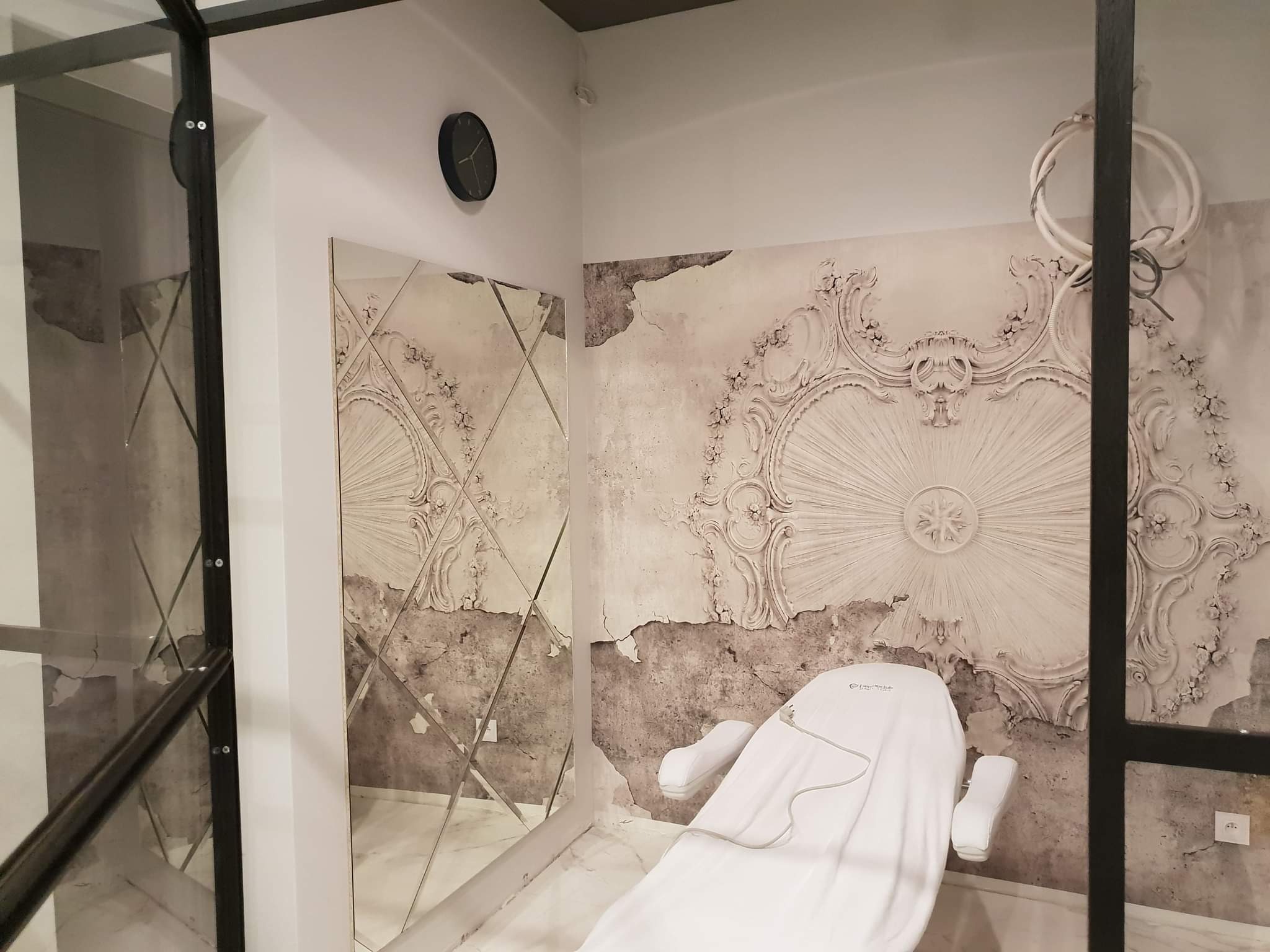 Pokój z lustrem w romby i dekoracyjną tapetą w stylu vintage, z białym fotelem kosmetycznym przykrytym pokrowcem.