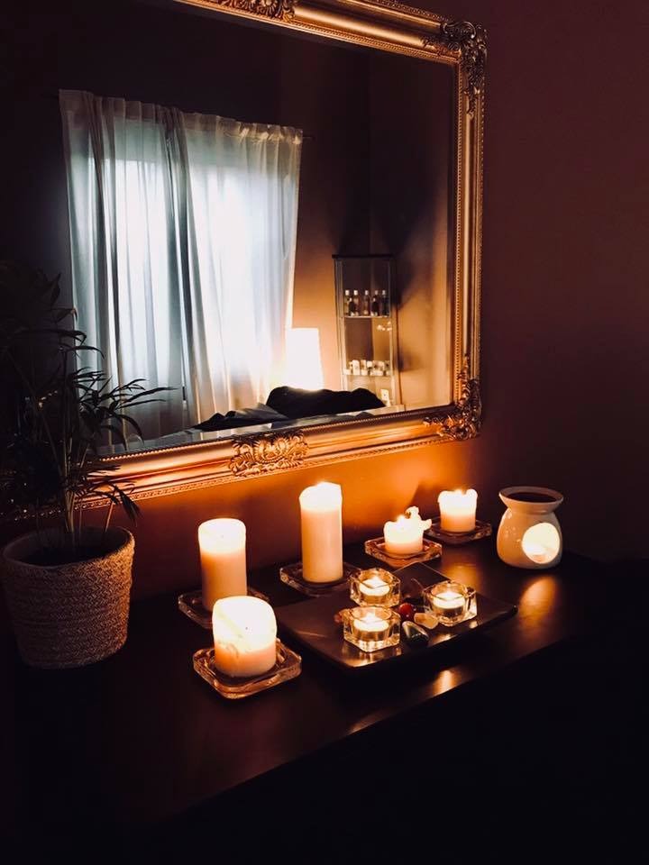 Ustawienie w gabinecie: zapalone świece na tacy, dyfuzor zapachowy i roślina doniczkowa przed lustrem w ozdobnej ramie, tworzące relaksującą atmosferę.