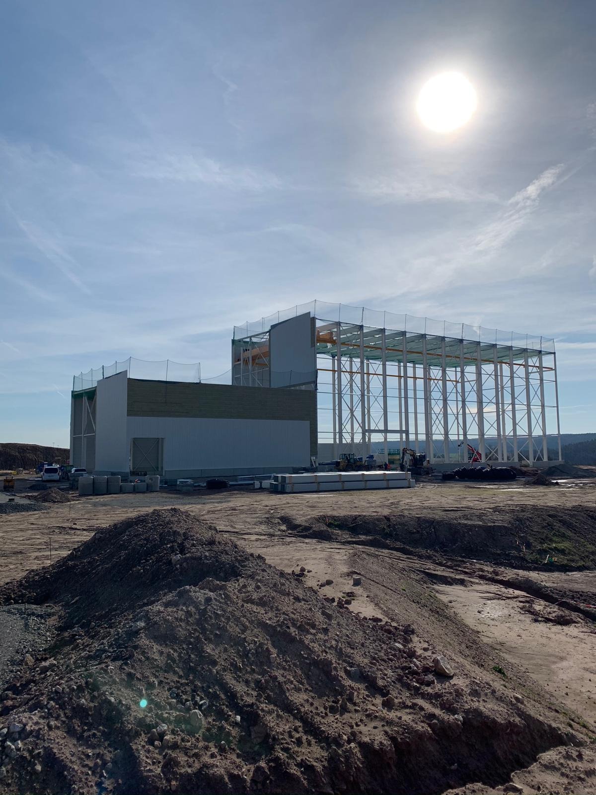 Budowa hali przemysłowej w Bolesławcu w trakcie montażu konstrukcji stalowej, widoczne elementy ścian i dachu, teren budowy z hałdami ziemi.