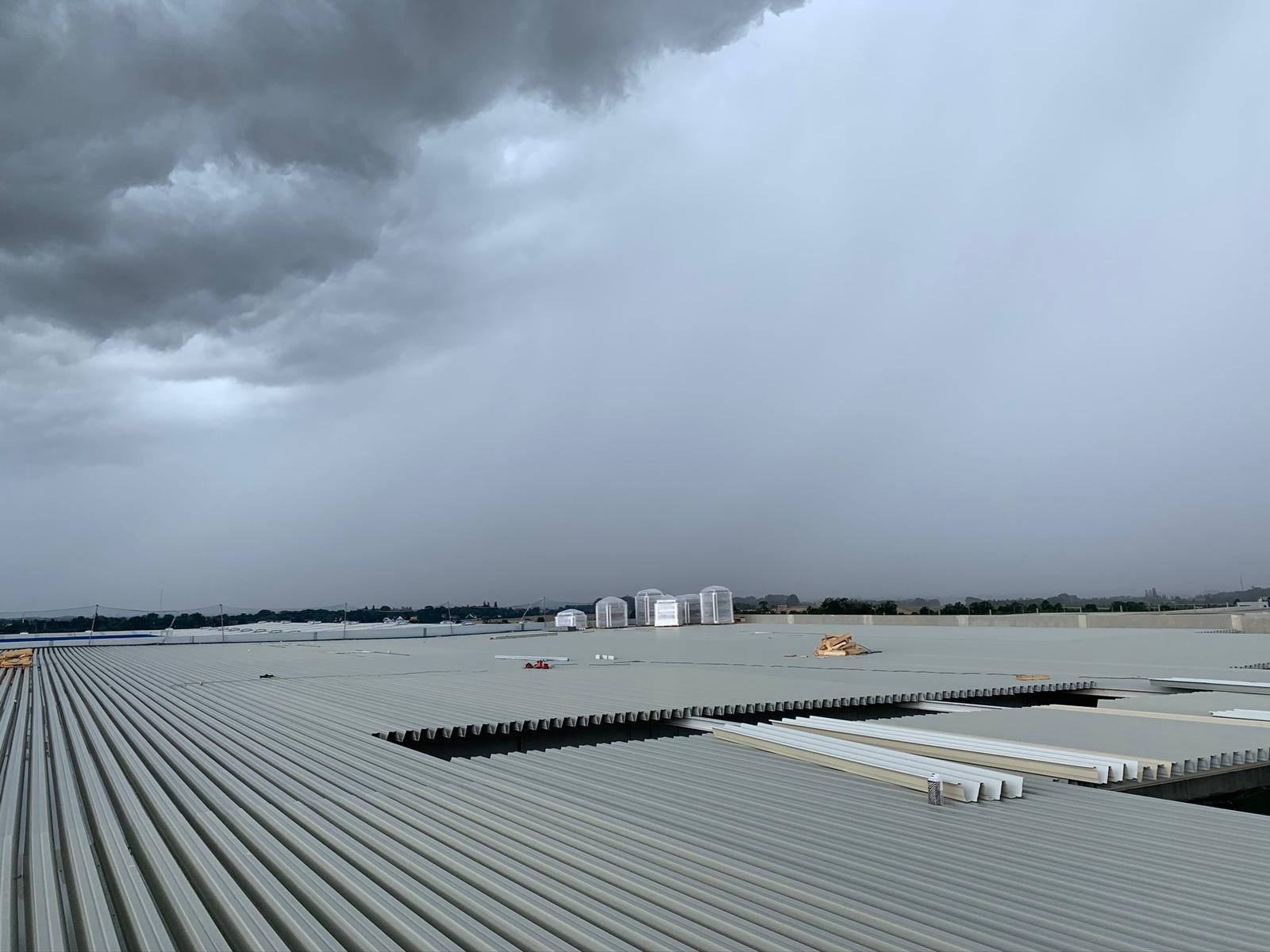 Montaż paneli na dachu przemysłowym w pochmurny dzień, widoczne elementy konstrukcyjne i materiały izolacyjne, w tle zbiorniki przemysłowe.