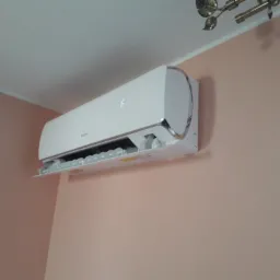 Zamontowany, biały klimatyzator z wyświetlaczem temperatury na różowej ścianie w pomieszczeniu z widocznym fragmentem karnisza.