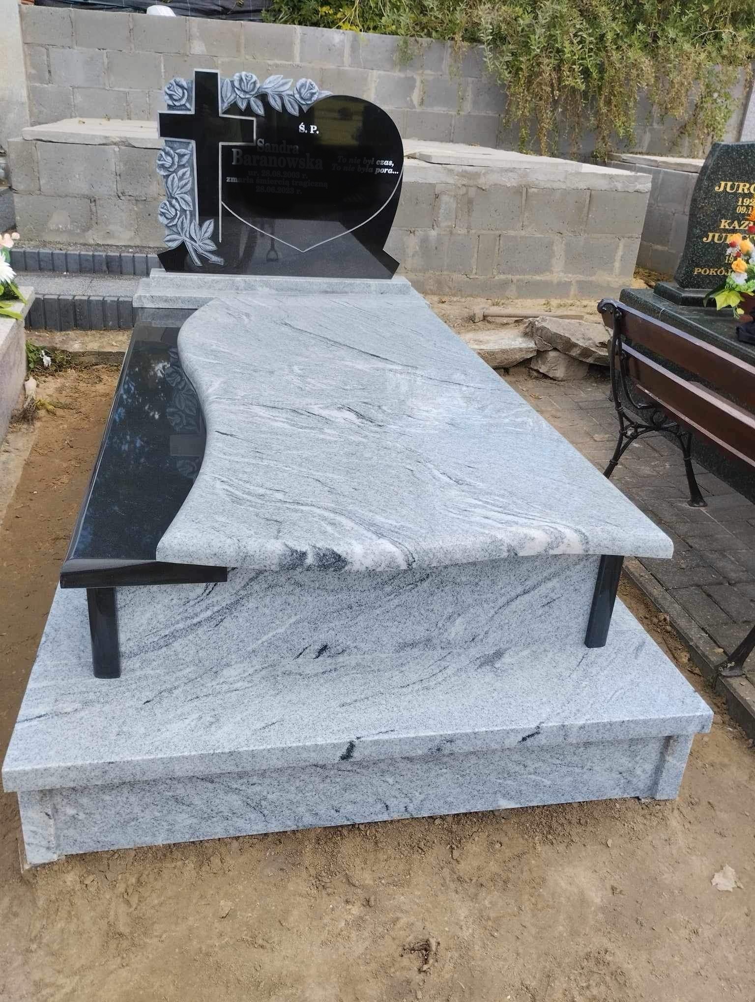 Granitowy pomnik nagrobny z czarnym krzyżem z motywem różanym i płytą z jasnego, wzorzystego kamienia, umieszczony na cmentarzu.