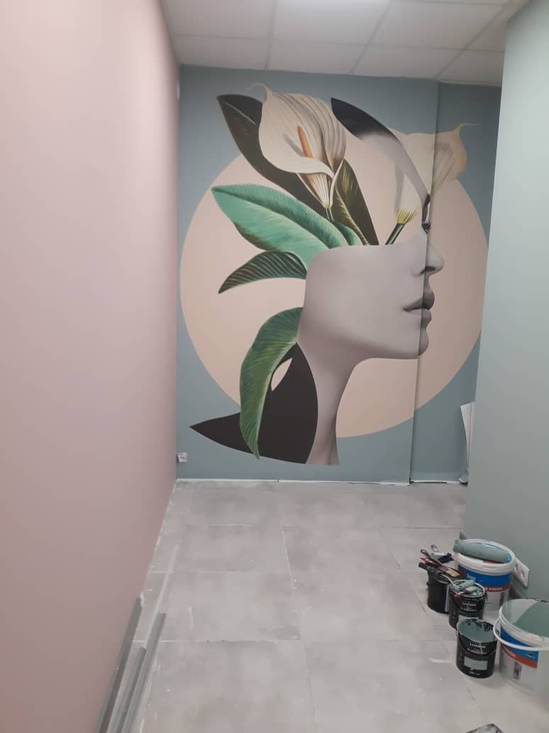 Ściana biura z artystycznym malunkiem przedstawiającym profil kobiety z kwiatami, widoczne pędzle i farby na podłodze, ściany w odcieniach różu i błękitu.