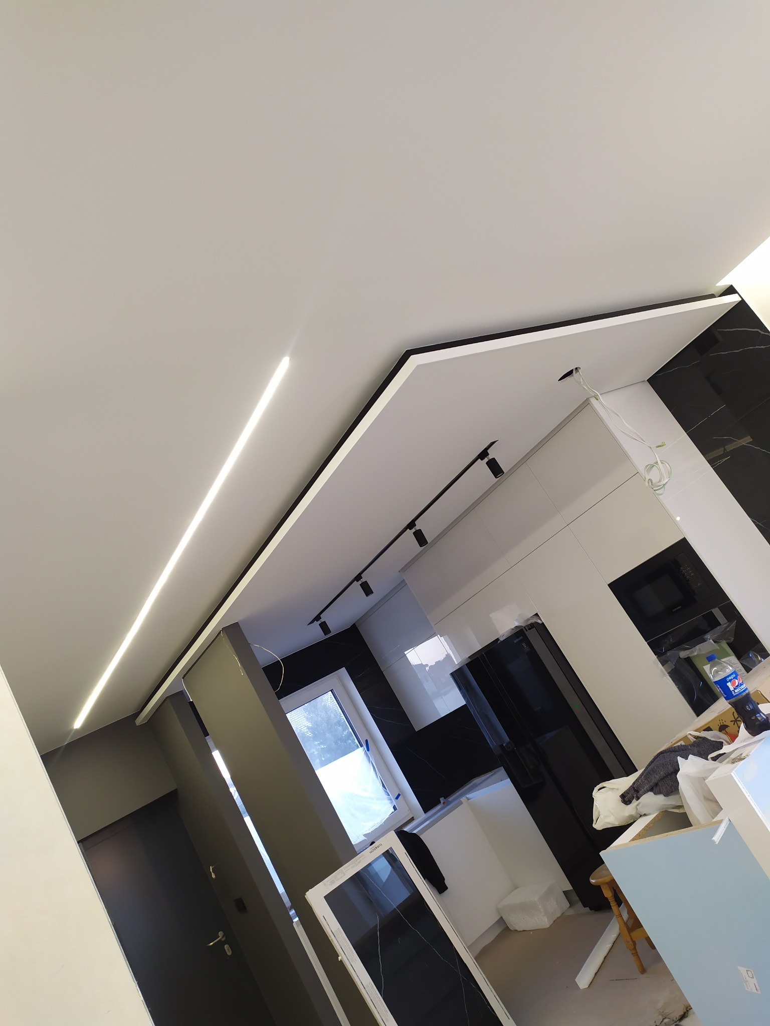 Montaż sufitu napinanego z oświetleniem LED w nowej kuchni z czarno-białymi płytkami i czarnymi elementami wyposażenia.