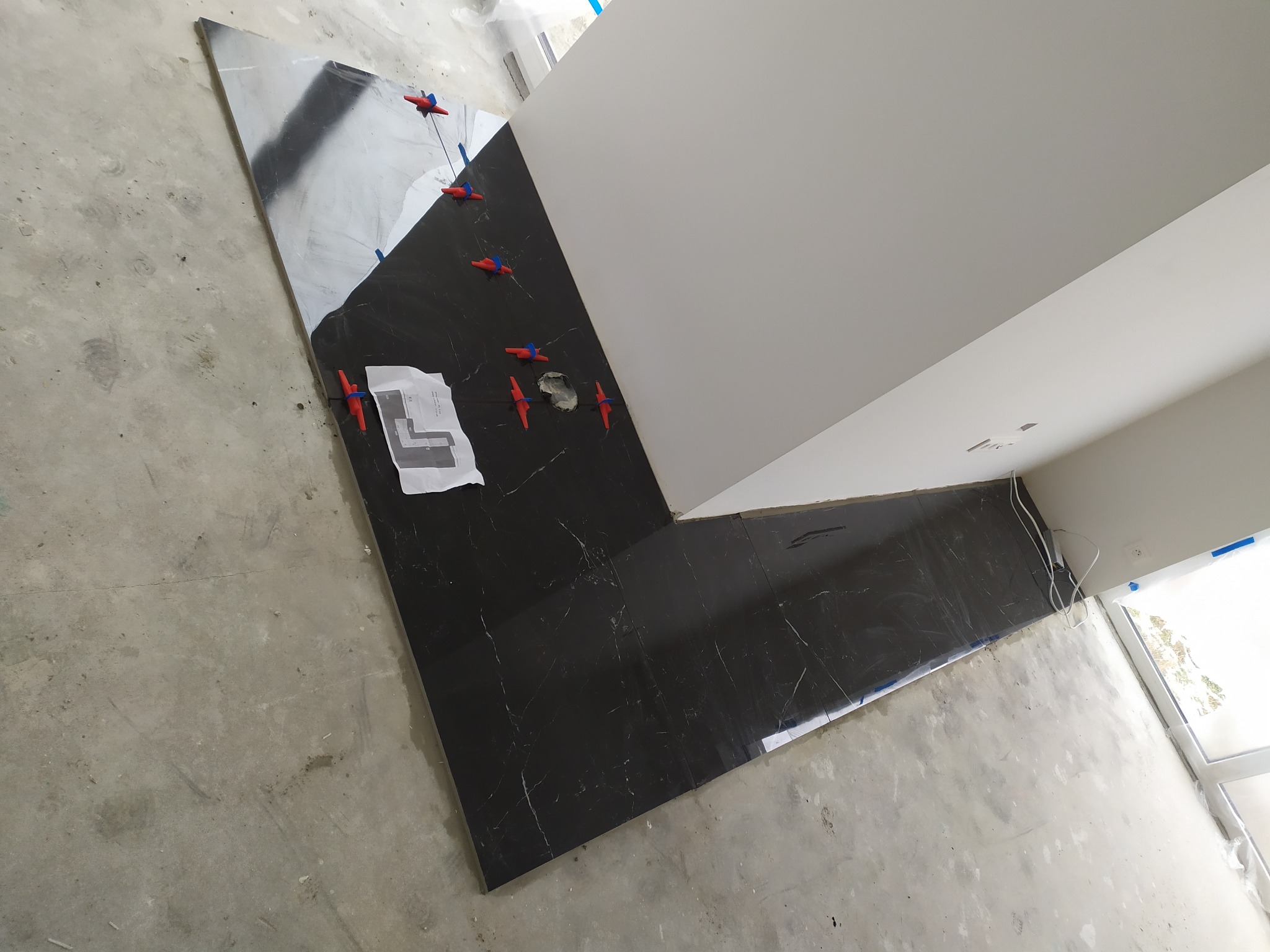 Układanie czarnych płytek podłogowych z białymi żyłkami, widoczne krzyżyki dystansowe i plan ułożenia płytek.