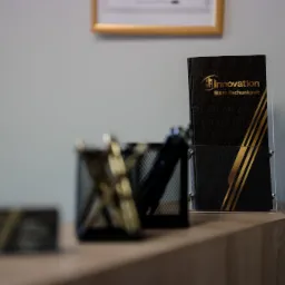 Ekspozycja materiałów informacyjnych biura rachunkowego Innovation, z logo w złotych barwach, na blacie w recepcji, z przybornikiem na długopisy w tle i certyfikatem na ścianie.
