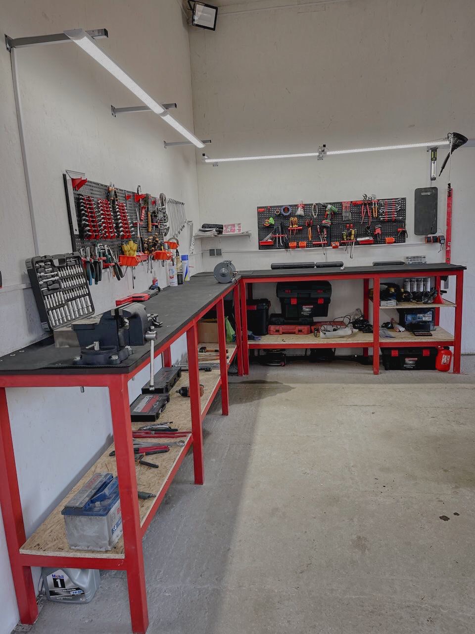 Warsztat z czerwonymi stołami roboczymi, narzędziami na ścianach i oświetleniem LED