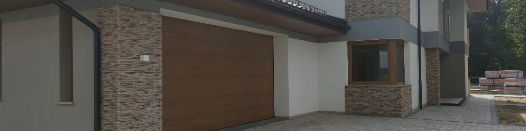 Nowoczesna brama garażowa segmentowa w kolorze drewna, zamontowana w elewacji budynku z elementami dekoracyjnymi z kamienia.
