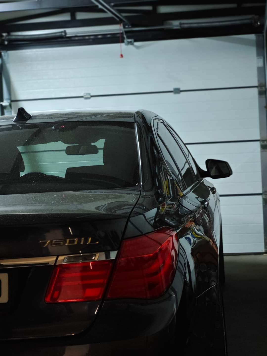 Czarny samochód BMW 750iL zaparkowany w garażu z białą segmentową bramą garażową w tle.