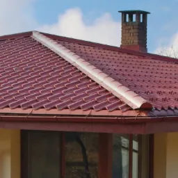 Czerwony dach z dachówki ceramicznej z kominem w tle, widoczne rynny i okno z odbiciem drzewa.
